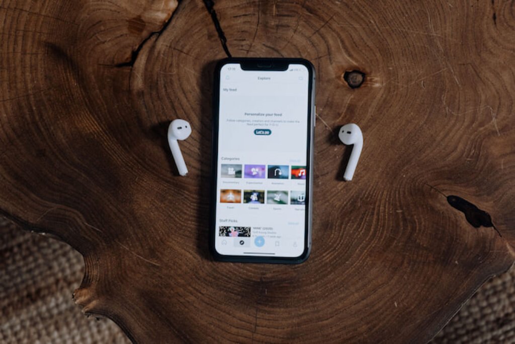 Um smartphone em cima da mesa com fones bluetooth ao lado.