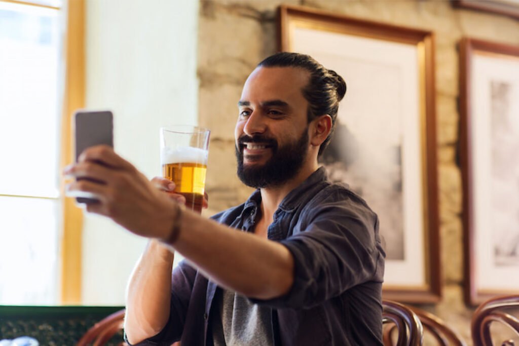 Uma pessoa tirando foto com um copo de cerveja nas mãos.