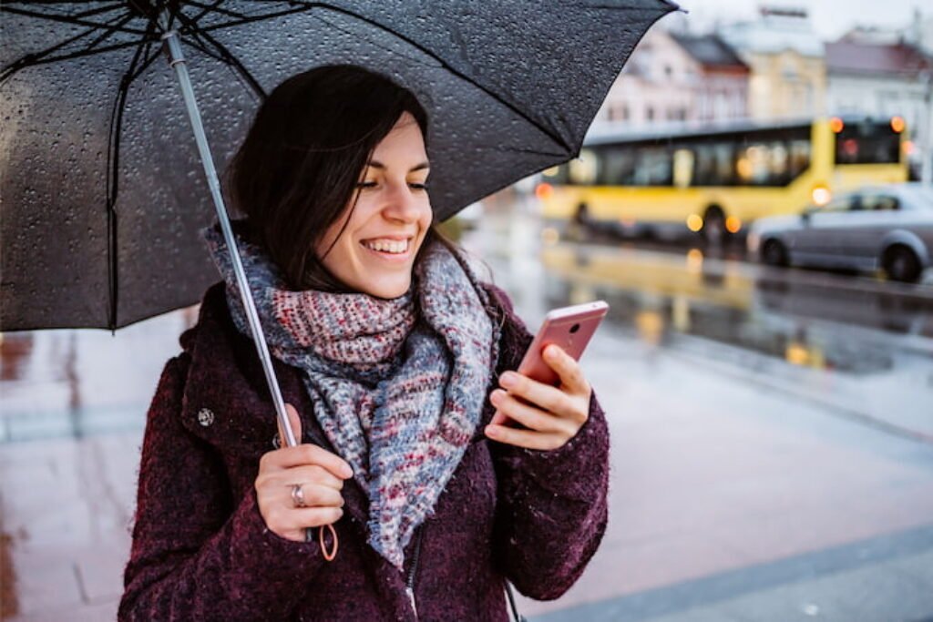 Uma pessoa olhando seu smartphone com guarda chuva na mão.